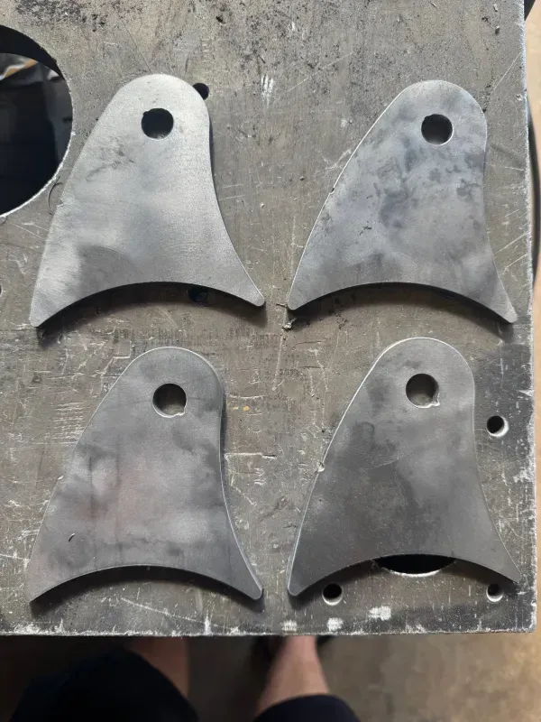 A laser cutter carves circular holes into a flat metal sheet, producing bright orange sparks.