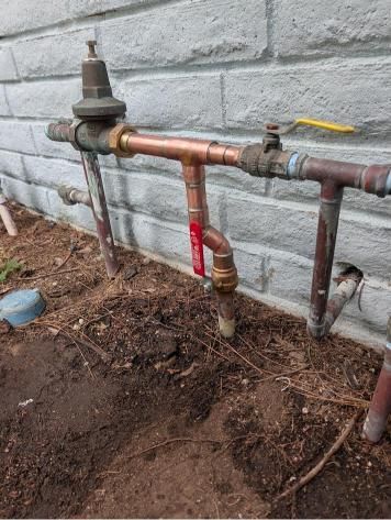 Outdoor copper and steel plumbing pipes with valves against a gray brick wall