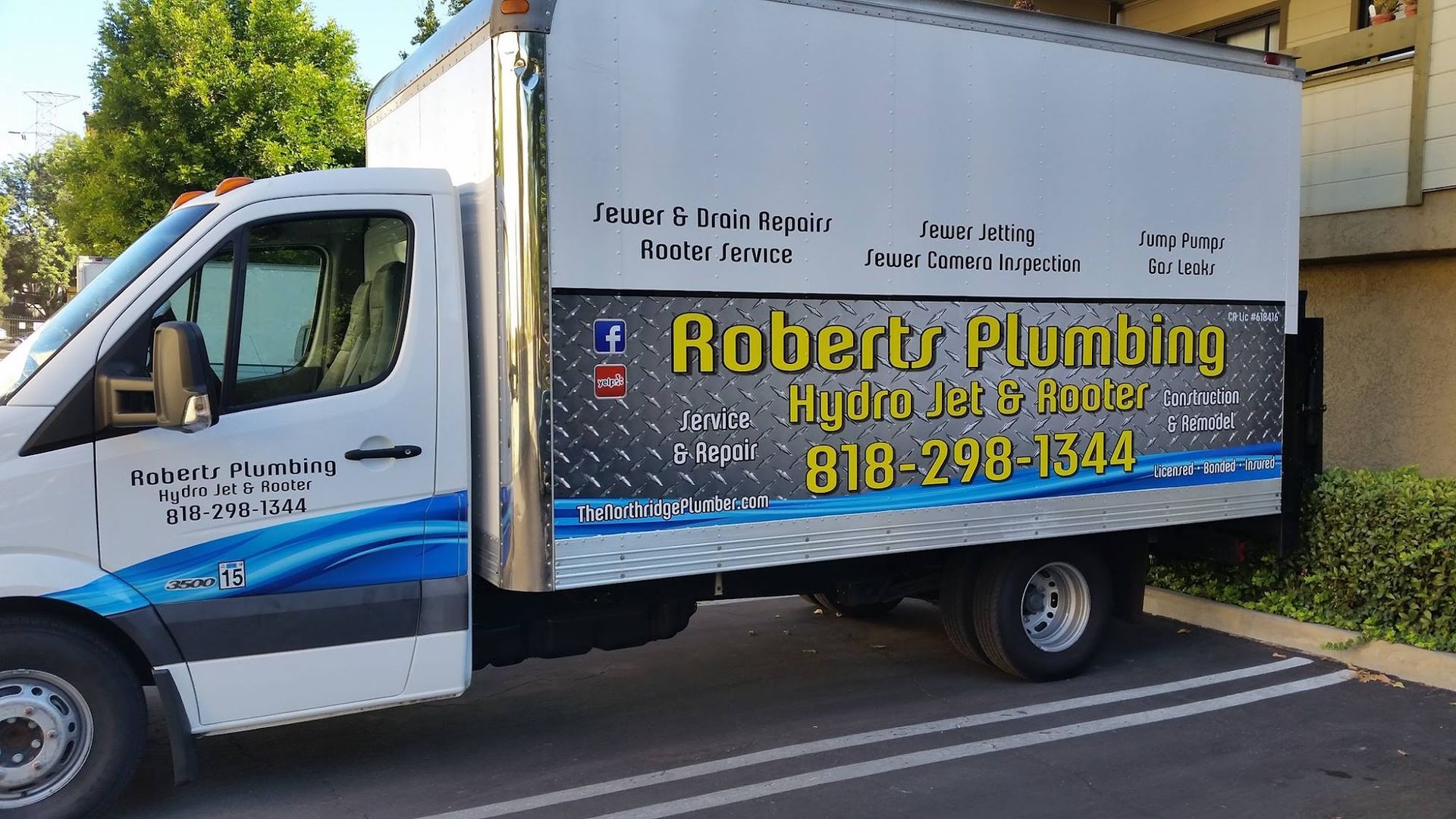 Roberts Plumbing truck parked outside. Blue and white lettering on a white truck. Contact info and social media logos.