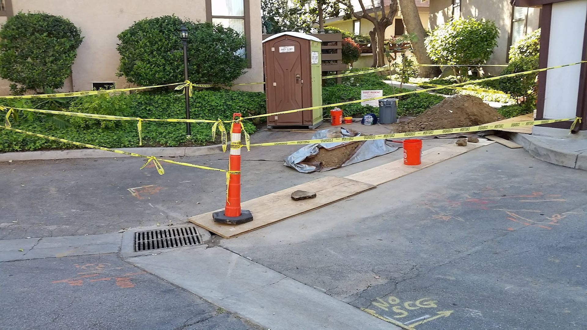 Construction site on a street, with caution tape, an orange cone, and a portable toilet.