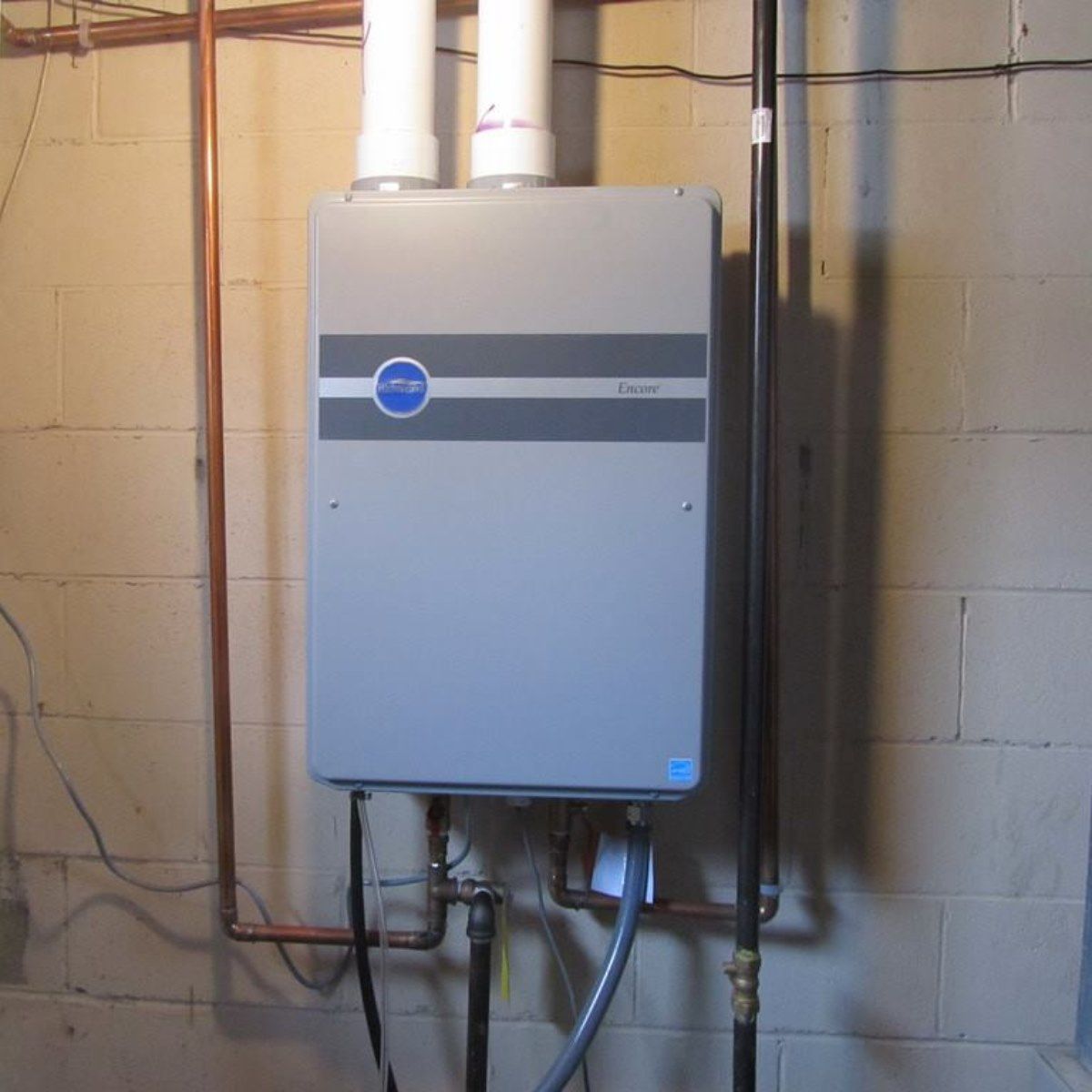 Gray tankless water heater mounted on a concrete wall with copper pipes.