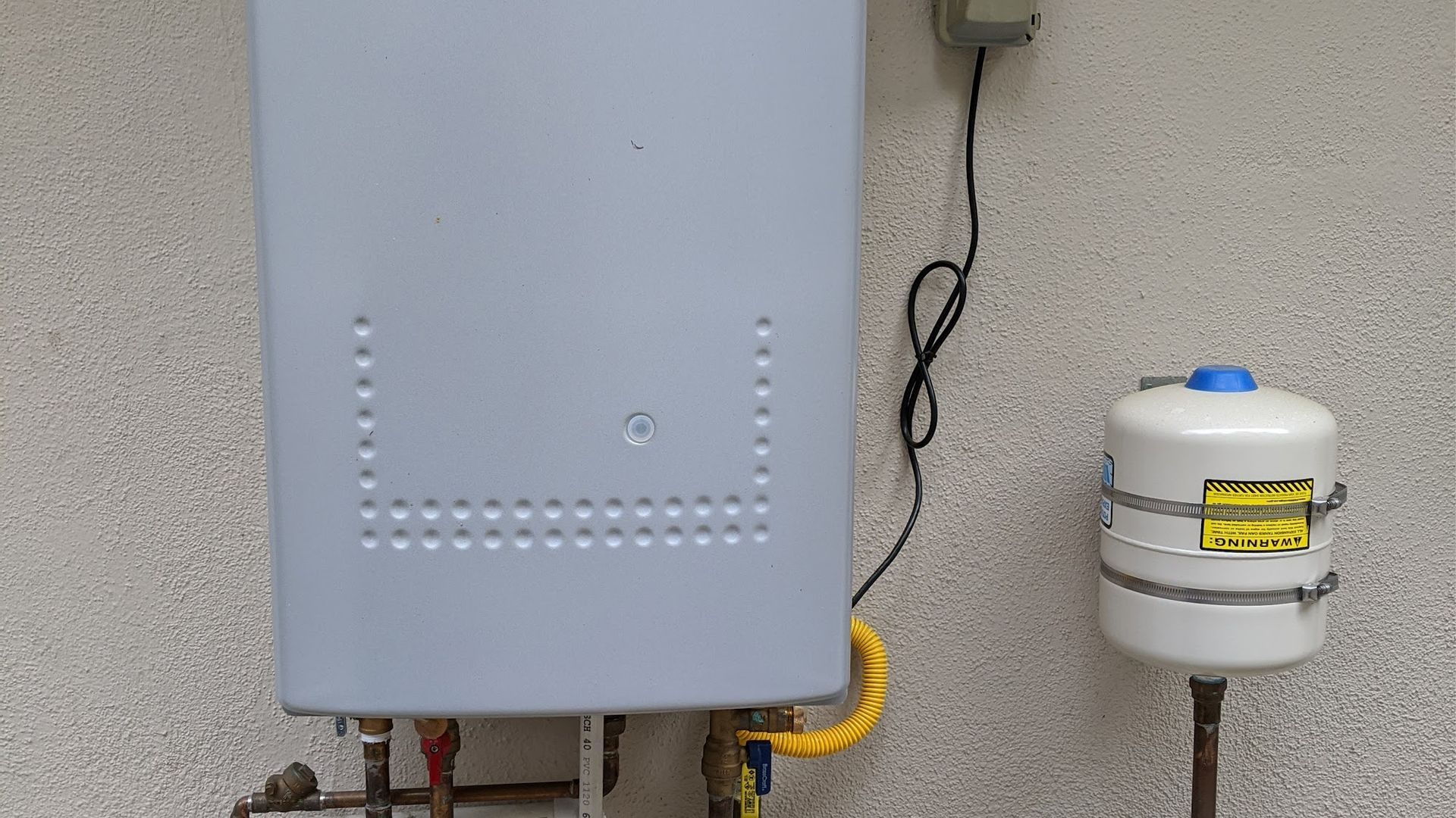 A gray water heater and a white expansion tank mounted on a wall.