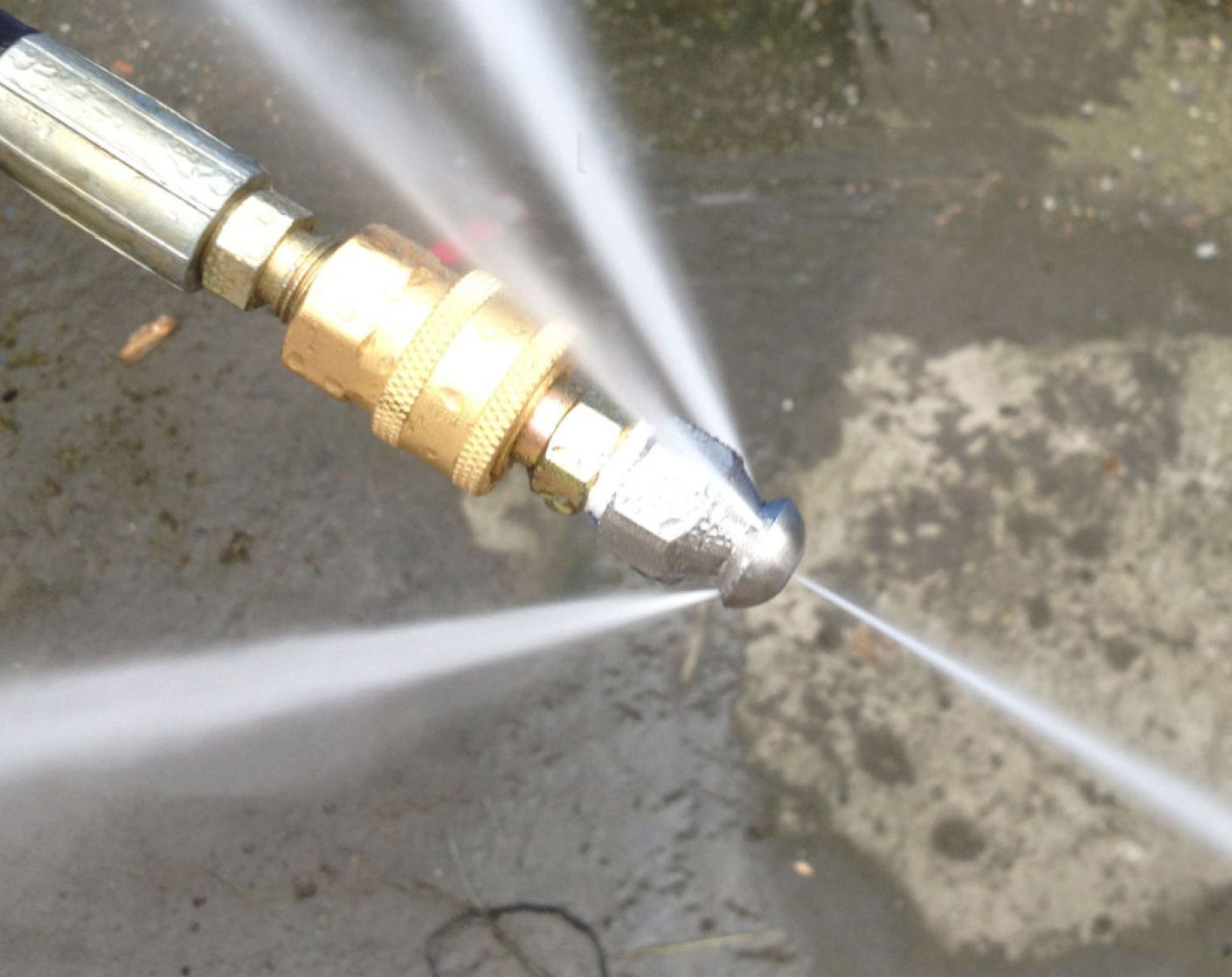 Close-up of a hose nozzle spraying water across a wet concrete surface.
