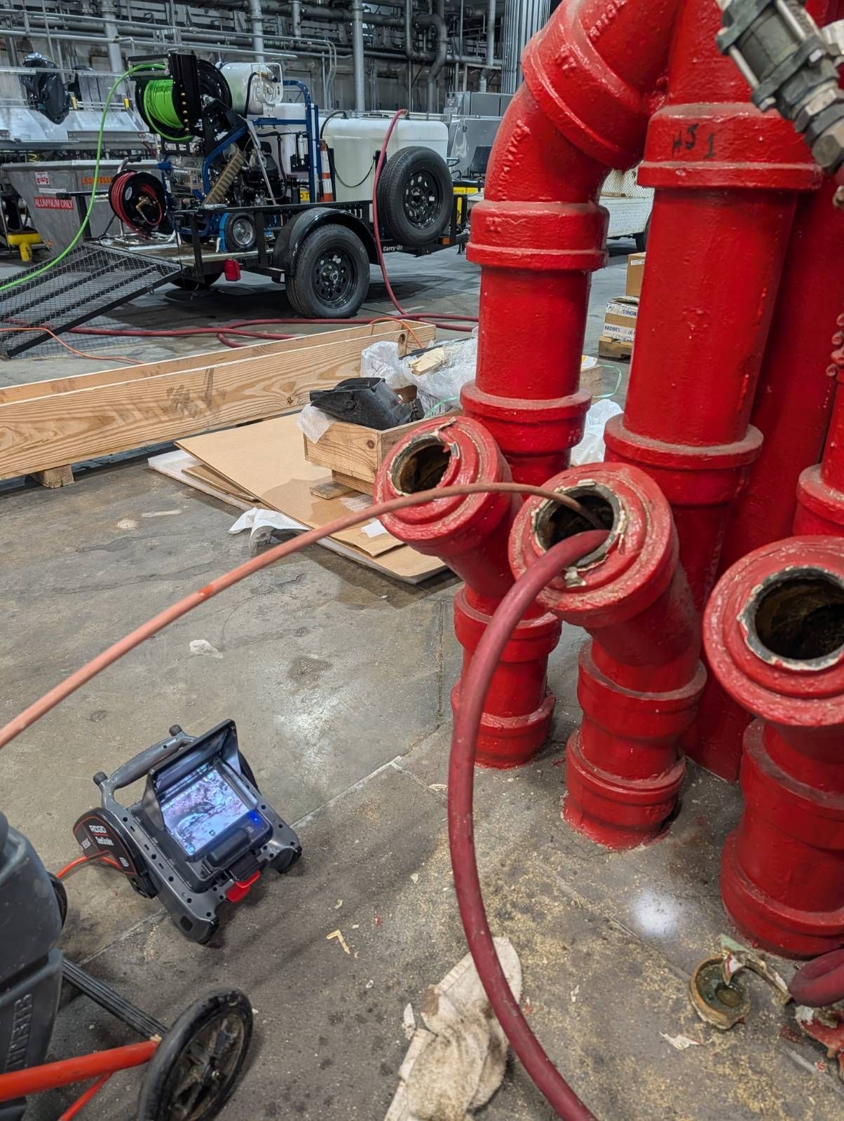 Industrial equipment with red pipes and hoses on a workshop floor, with a wheeled cart and tools nearby