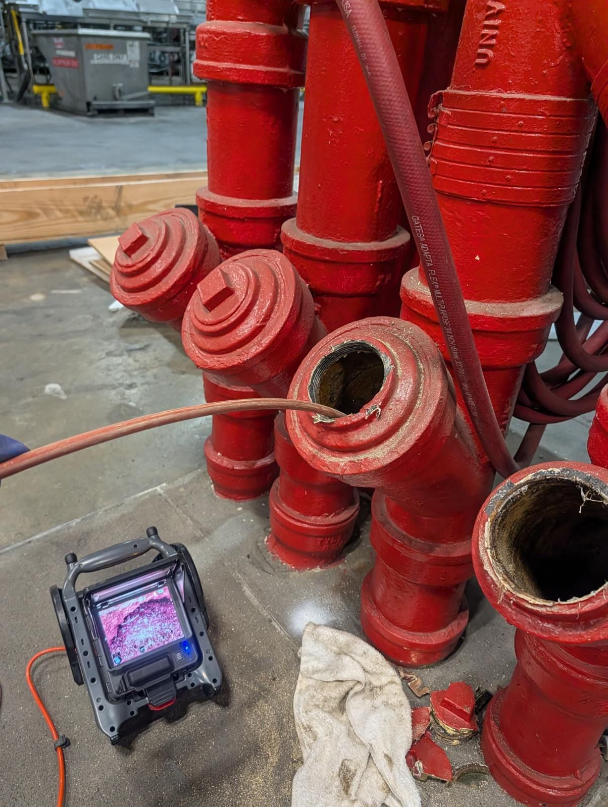 Red industrial pipes and fittings stacked on wet pavement, with a tablet on the ground nearby.