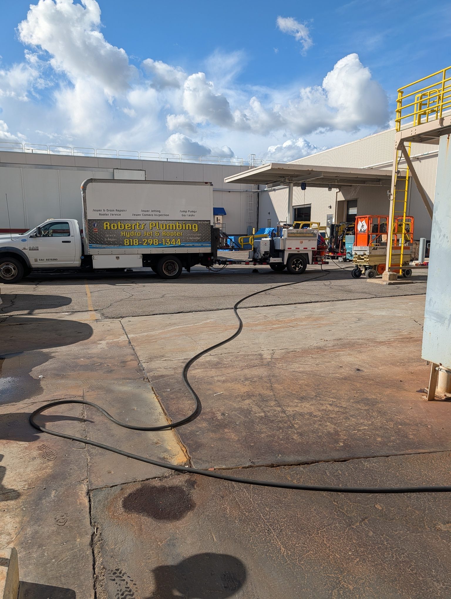 Truck and utility vehicles in an industrial yard with hoses on the ground under a partly cloudy sky