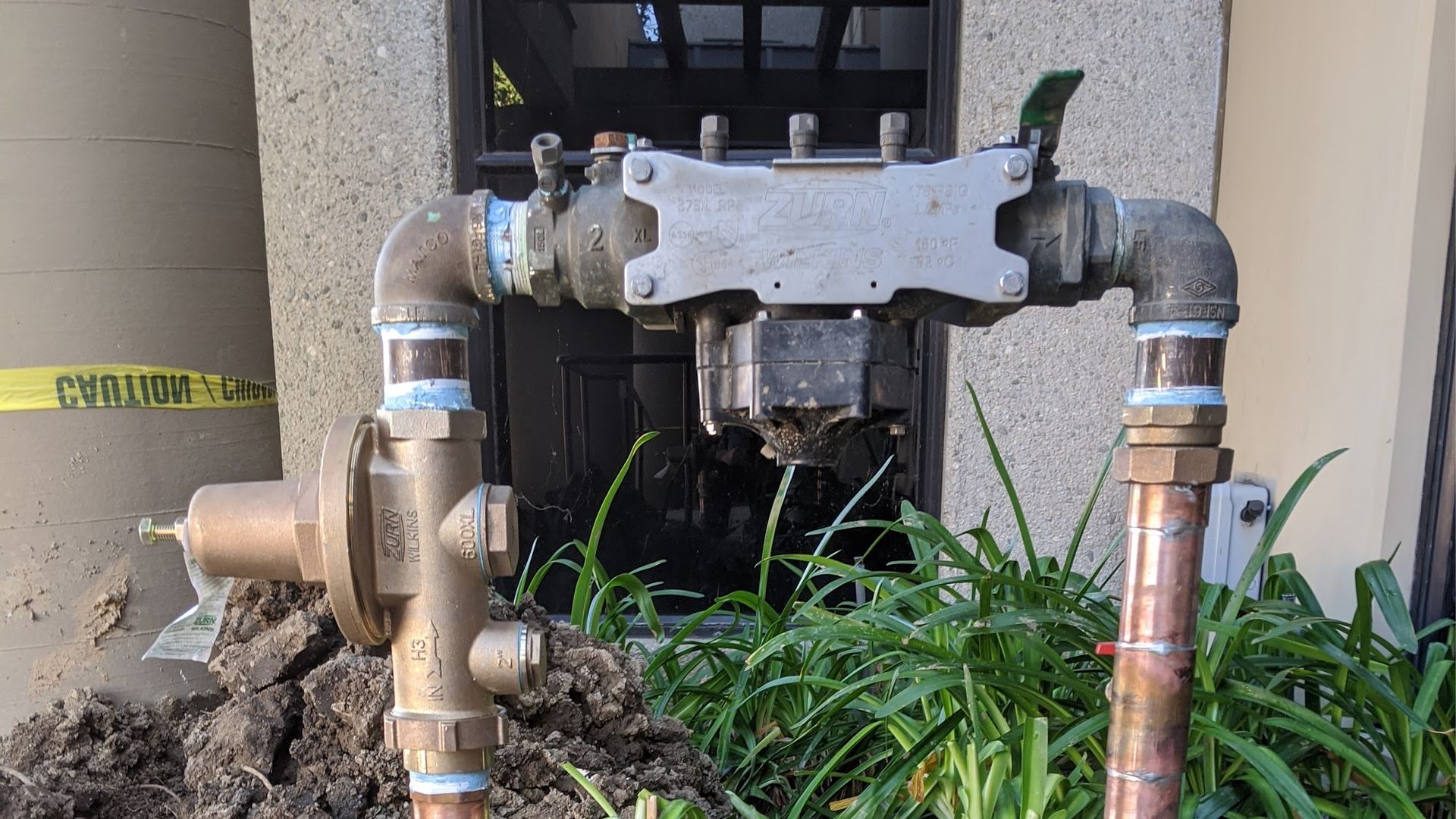 Water meter with pipes, a black box, and a leaking valve outdoors.