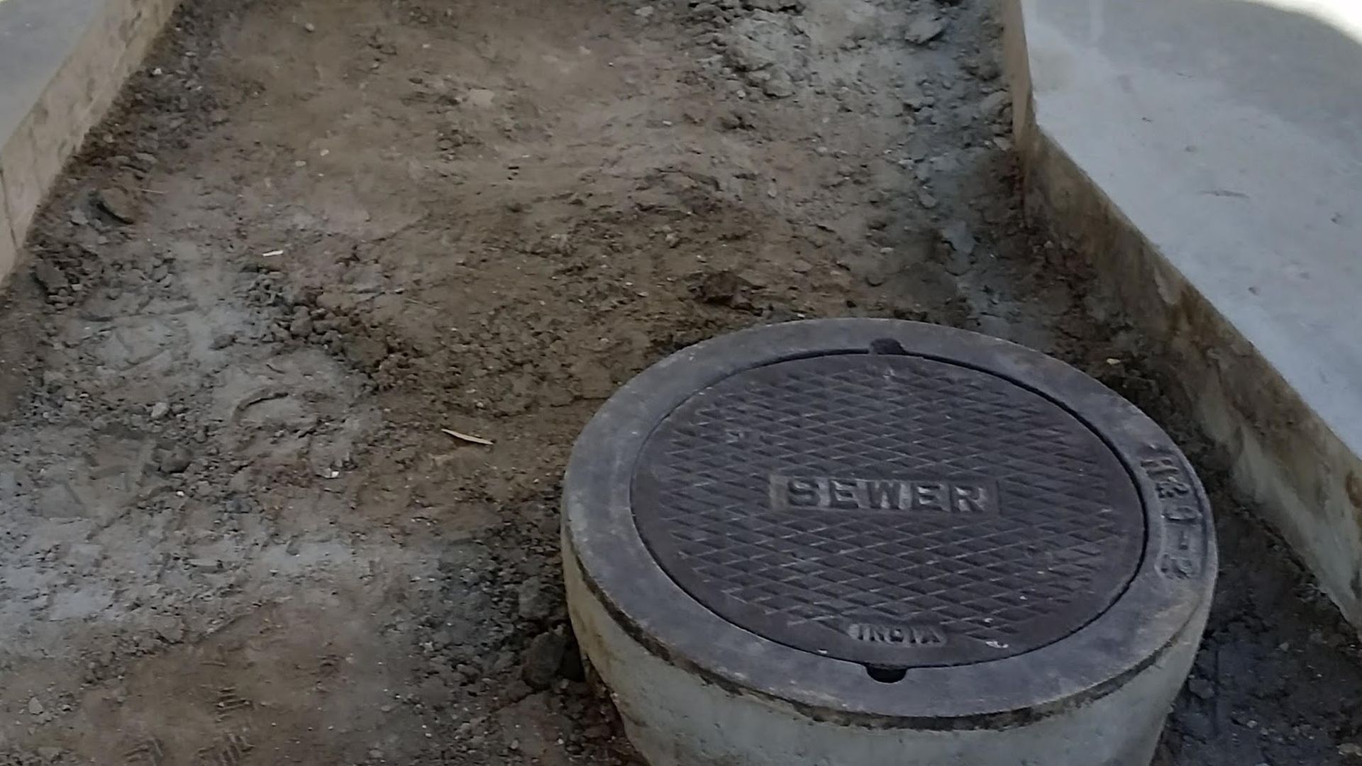A sewer manhole cover on a concrete ring set in dirt.