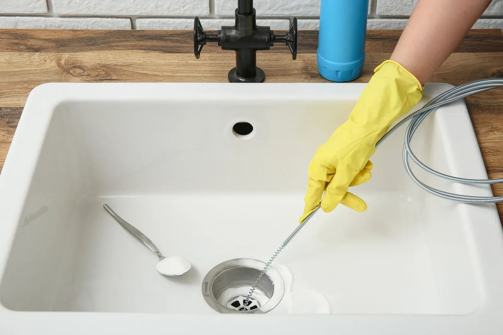 Person in yellow gloves cleaning a kitchen sink drain with a flexible brush