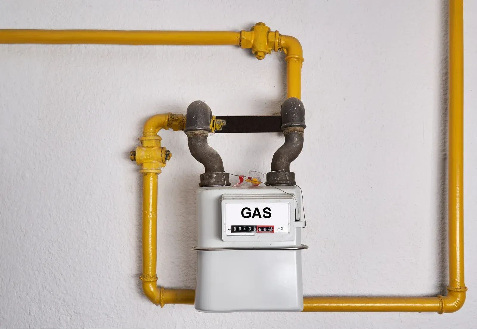 Gas meter with yellow pipes mounted on a white wall