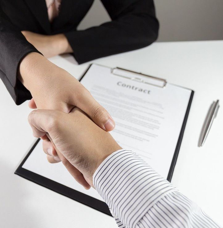 A man and woman shaking hands in front of a clipboard that says contract