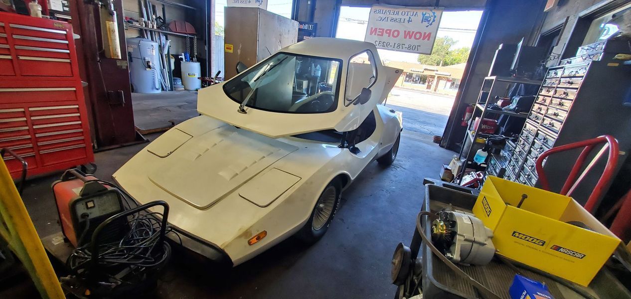 A white car is parked in a garage with its hood up.