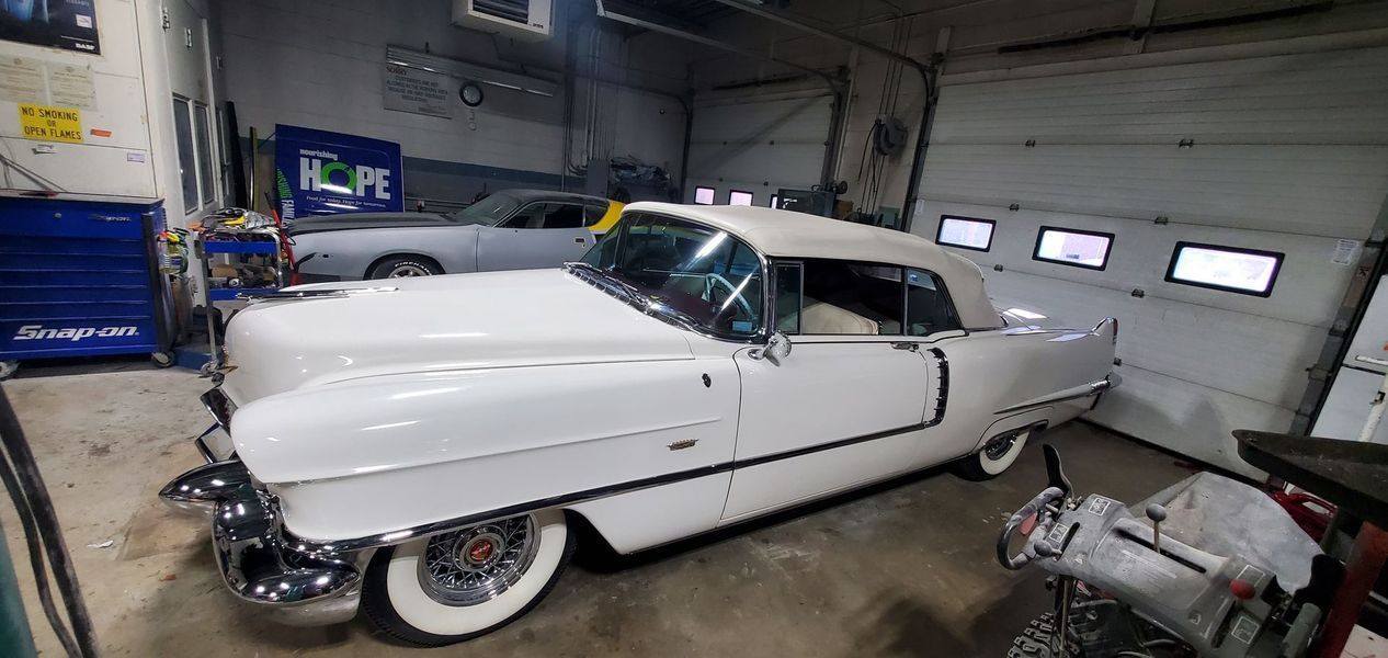 A white cadillac is parked in a garage next to a garage door.