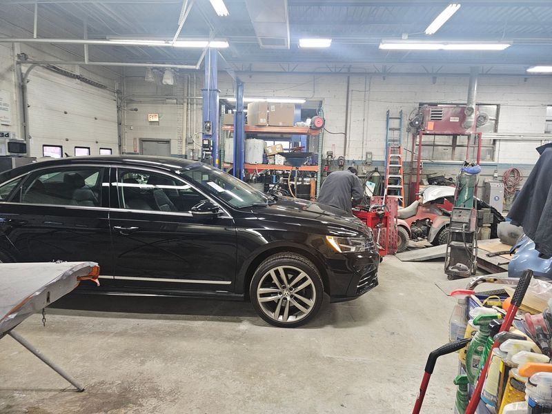 A black car is parked in a garage with a man working on it.