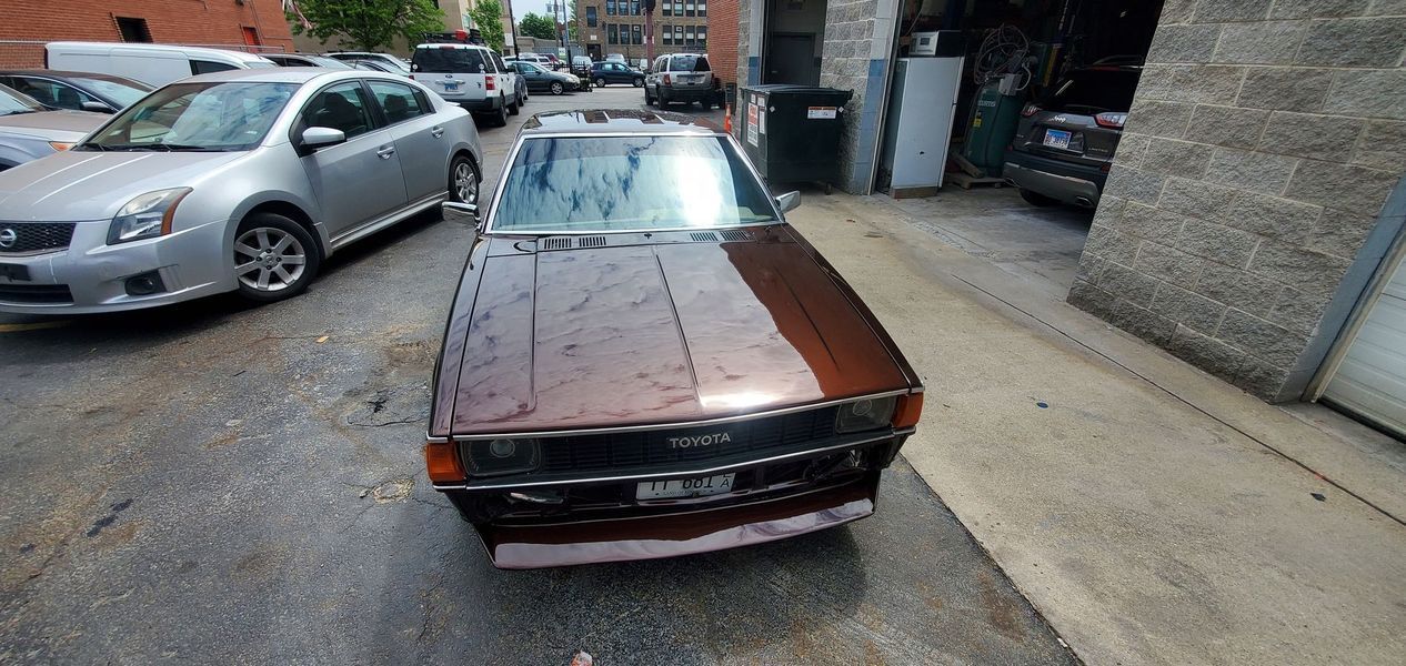 A brown car is parked in a parking lot next to a silver car.