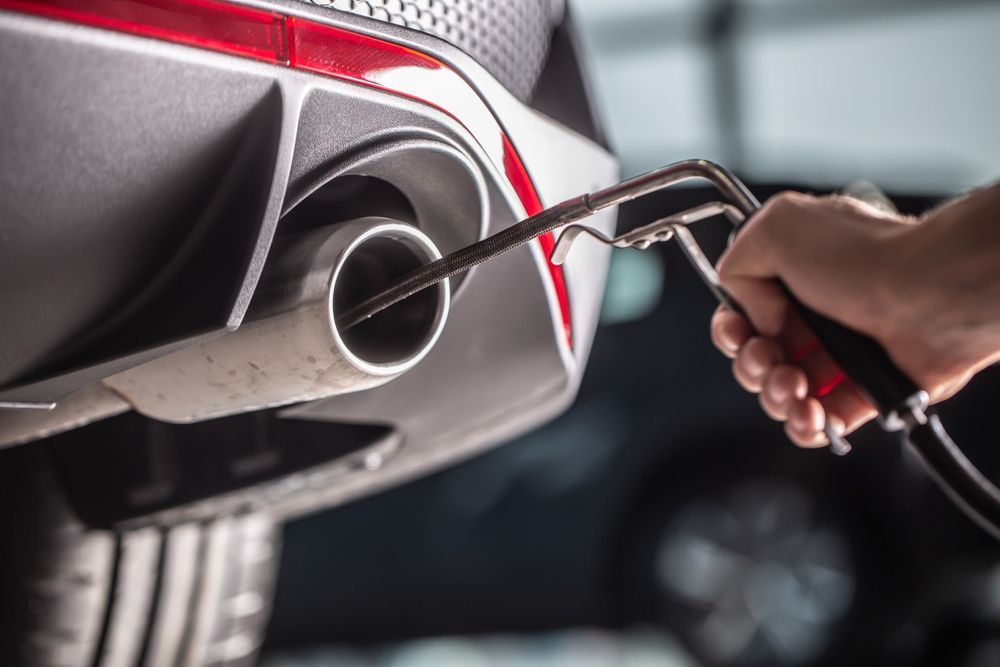 A person is blowing air into the exhaust pipe of a car.