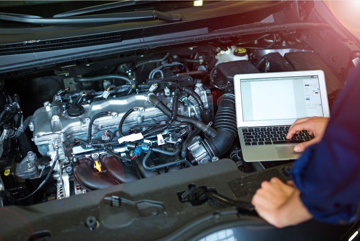 A mechanic is using a laptop to check the engine of a car.
