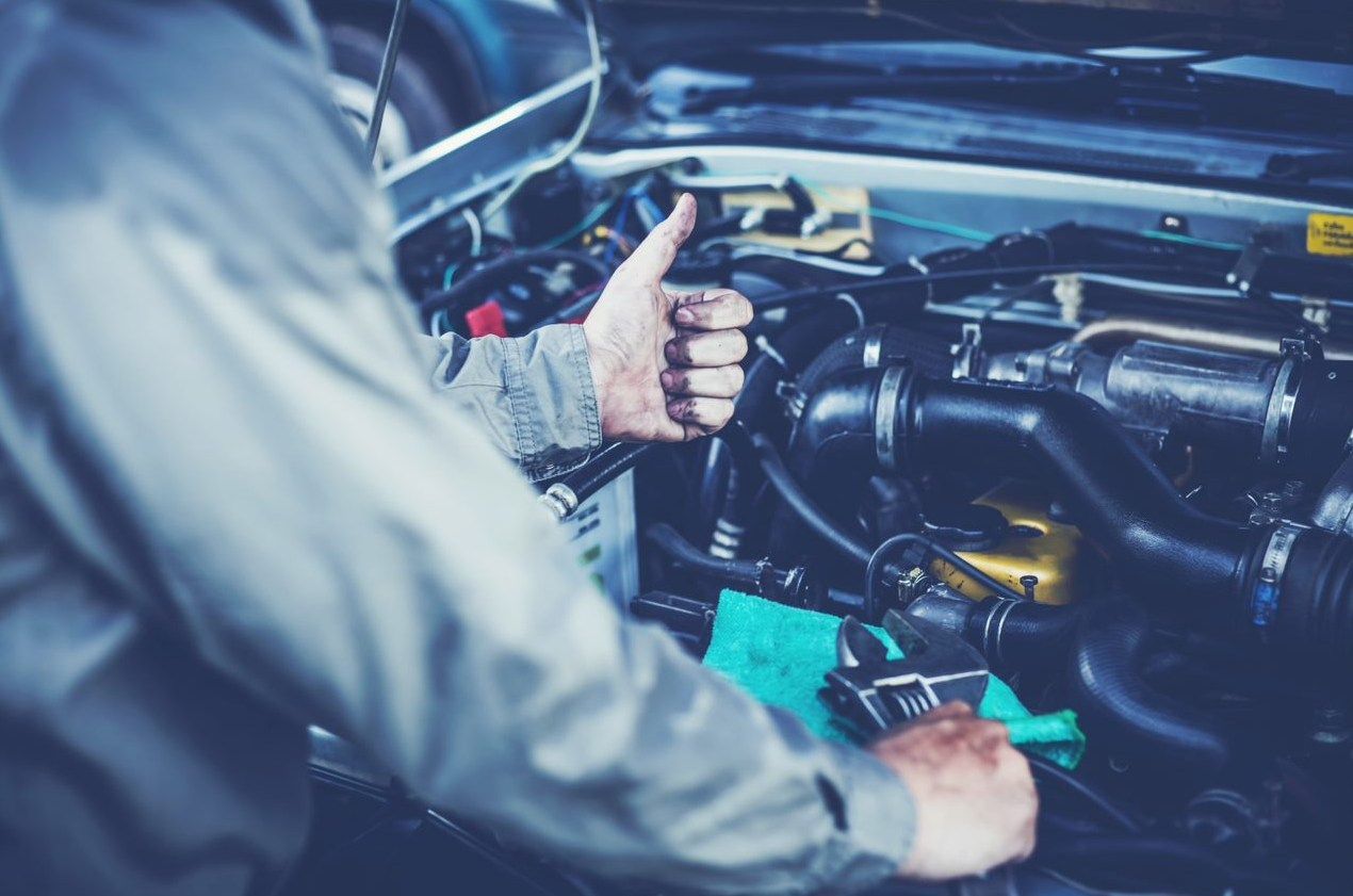 A man is working on a car engine and giving a thumbs up.