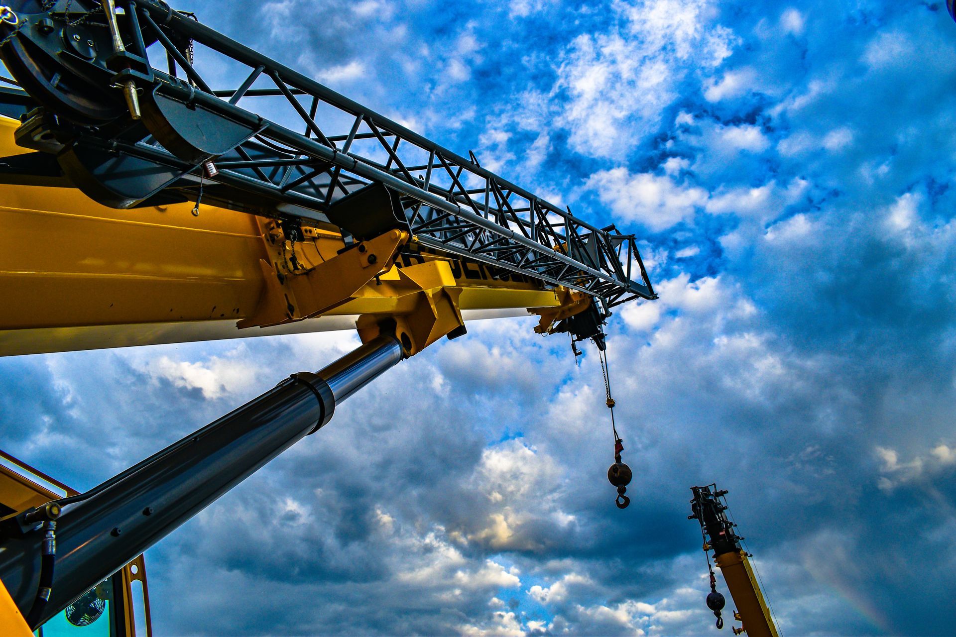 Yellow crane boom against a cloudy sky, lifting something.
