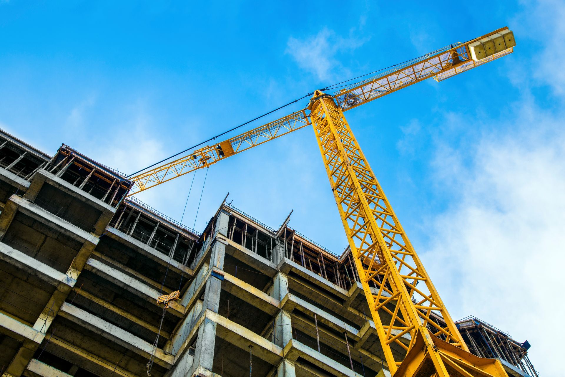 Yellow construction crane next to a partially built concrete building under a blue sky.