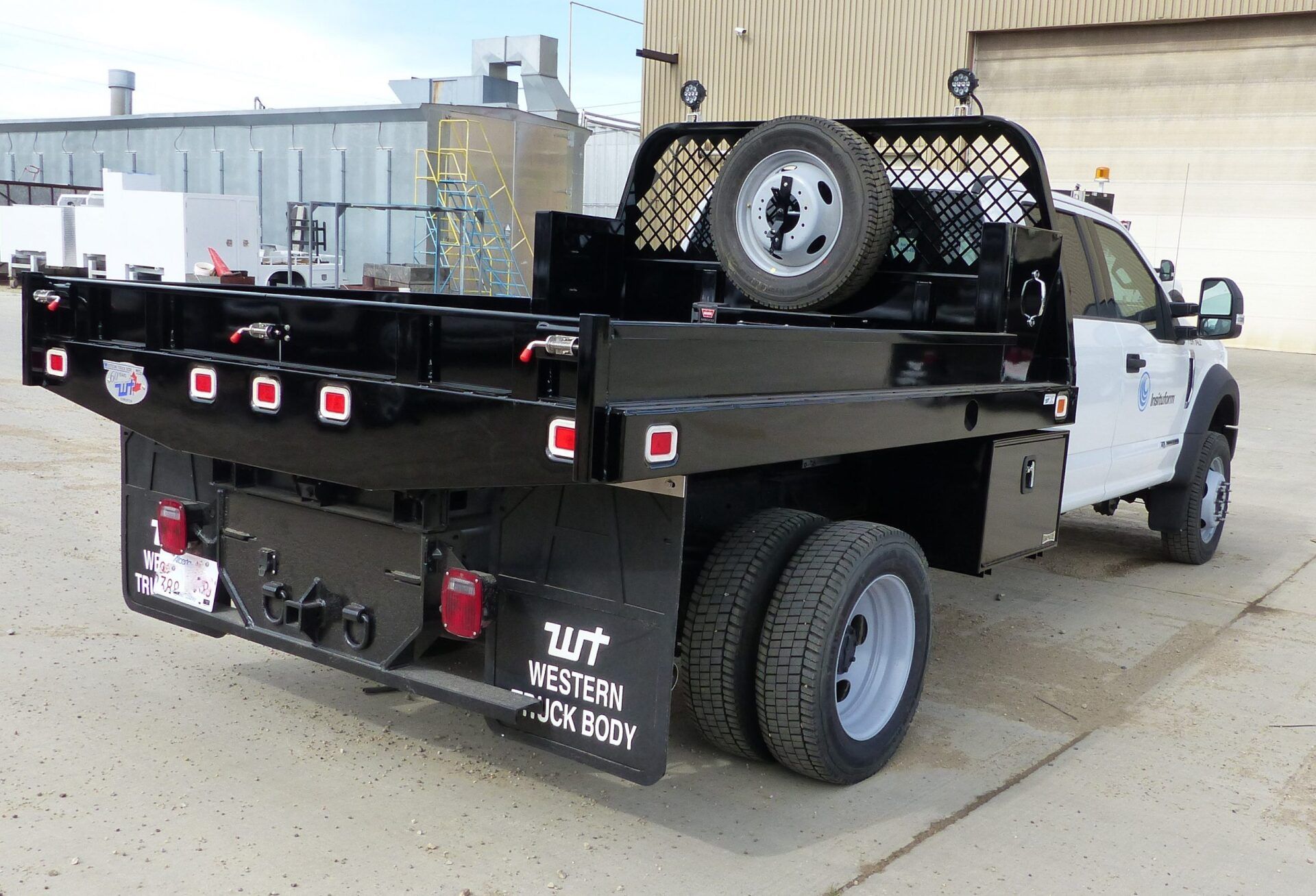 A white pickup truck with a black Western Truck Body dump bed parked outdoors on a paved lot.
