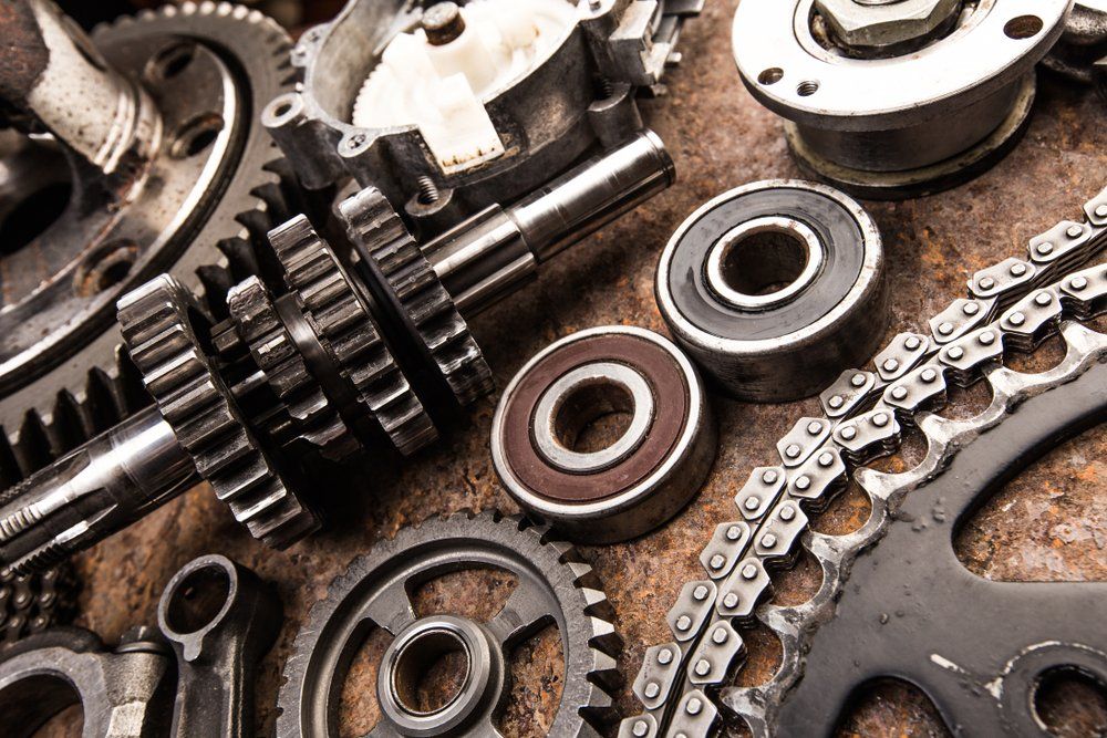 A pile of metal gears , bearings , chains and other parts on a rusty surface.