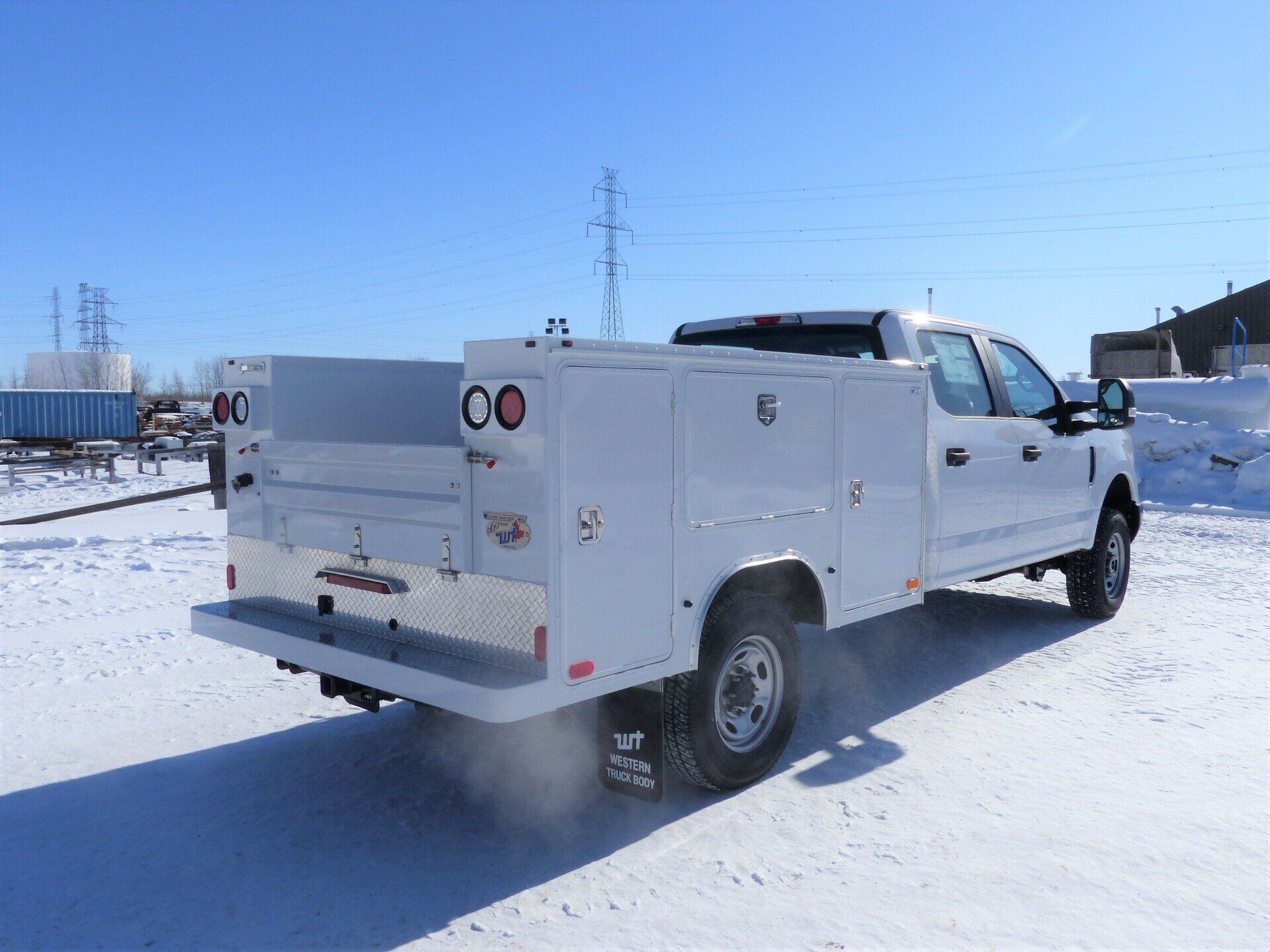 White utility truck with a service body parked on snow-covered ground under a clear blue sky.