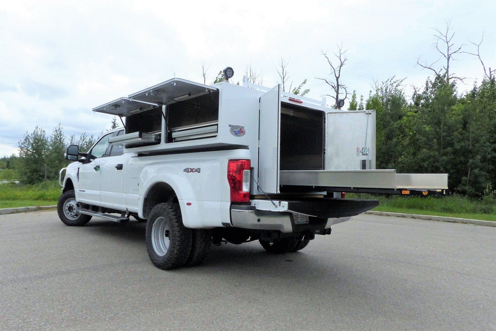A white utility truck parked outdoors with a large, open storage compartment and a pull-out shelf extending from the back.
