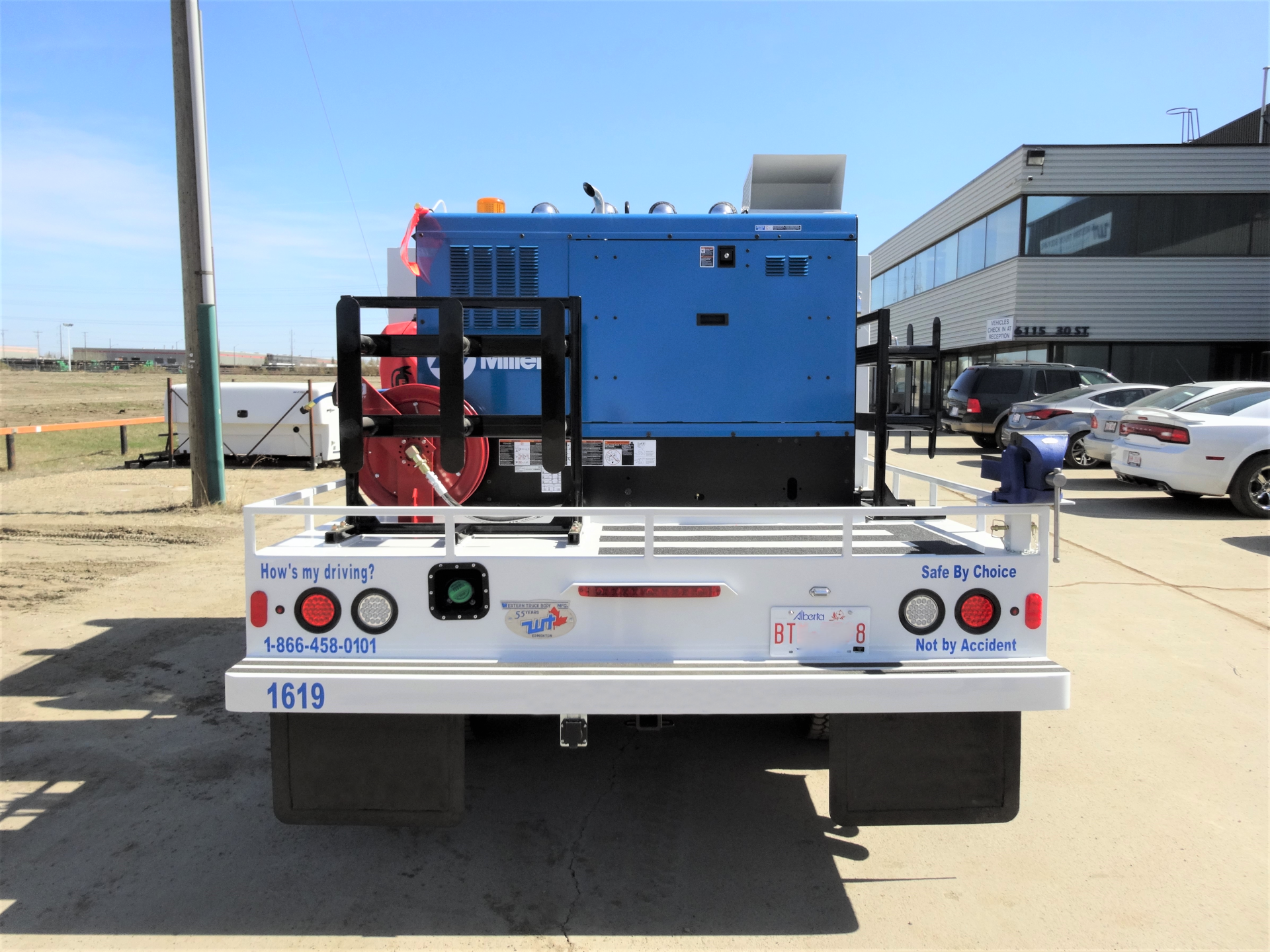 Rear view of a white service truck with blue generator on flatbed, parked outdoors.