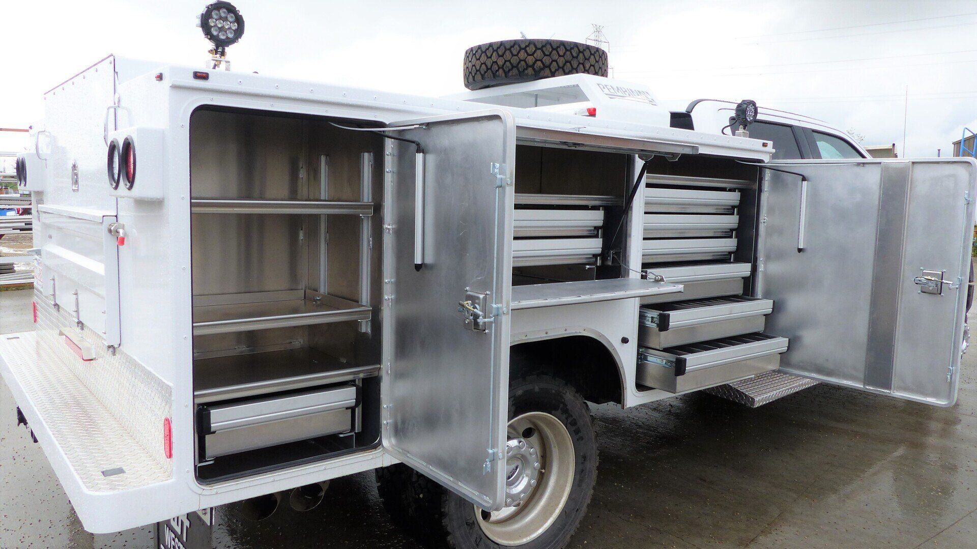 White service truck with its side storage compartments and metal drawers fully opened in an outdoor lot.