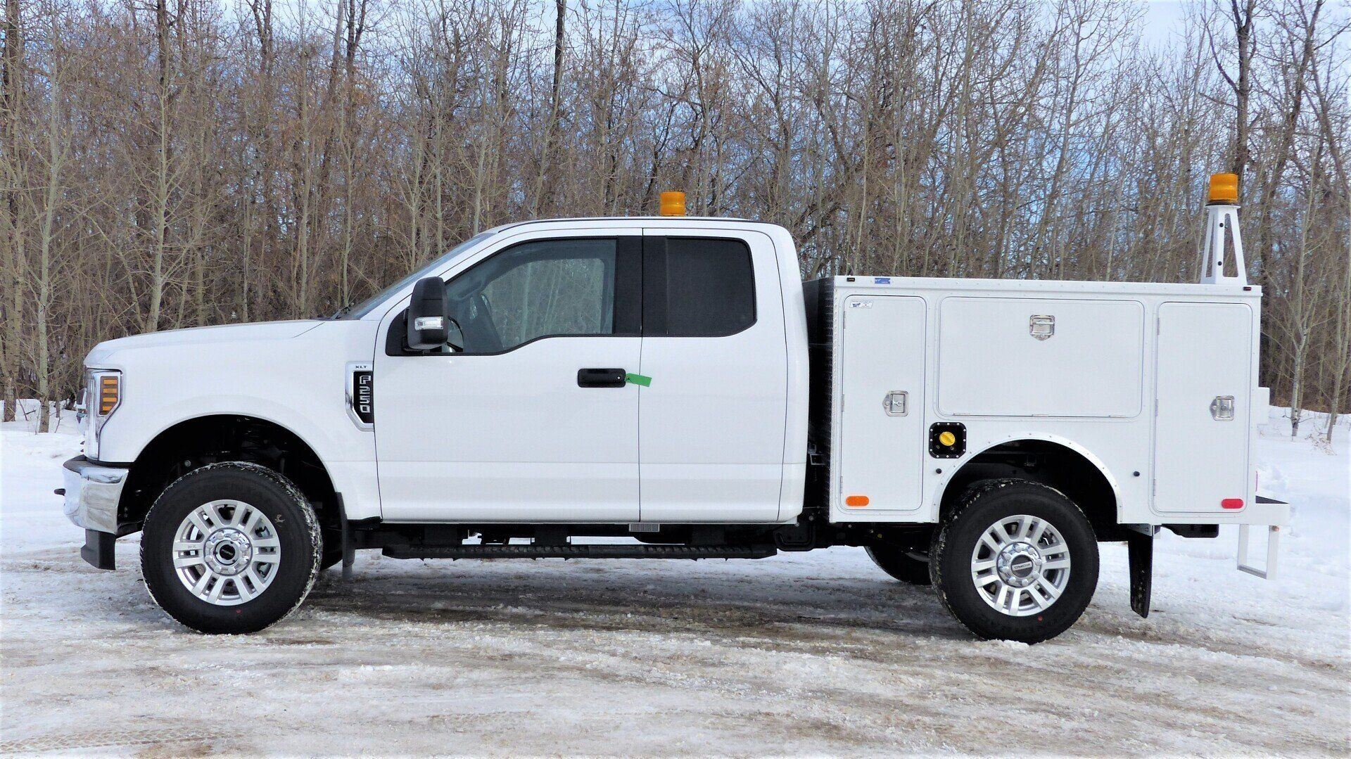White Ford F-Series work truck with a utility bed, parked in a snowy forest setting with orange warning beacons.