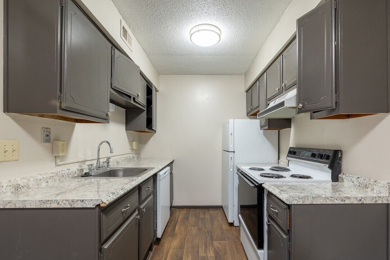 Kitchen with gray cabinets, white appliances, and speckled countertops.