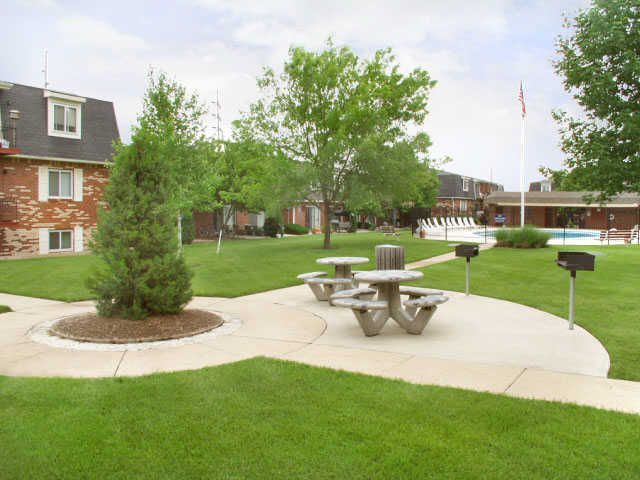 Grassy courtyard with picnic tables, trees, a pool, and brick apartment buildings.