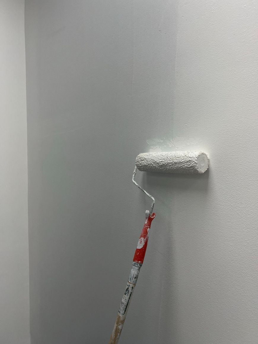 Paint roller applying white paint to a gray wall corner