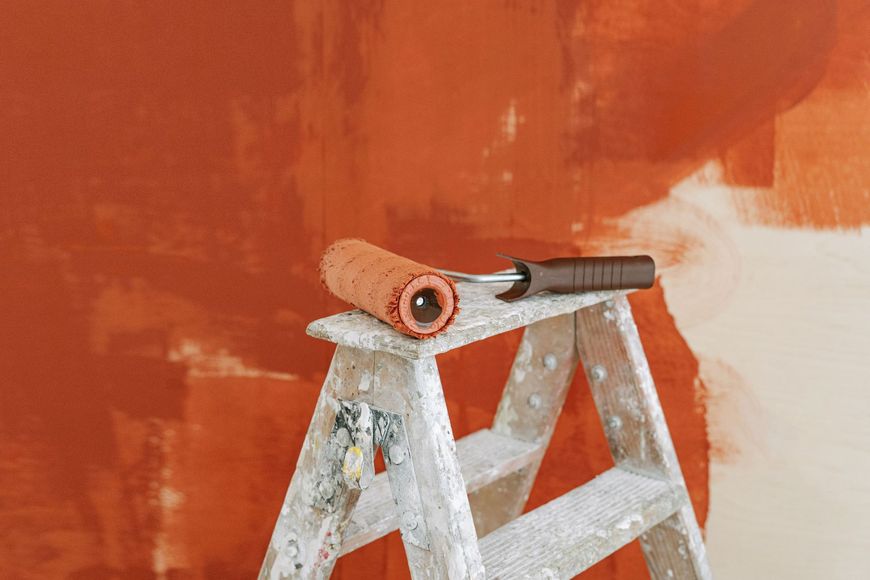 Paint roller on a step ladder in front of an orange-painted wall