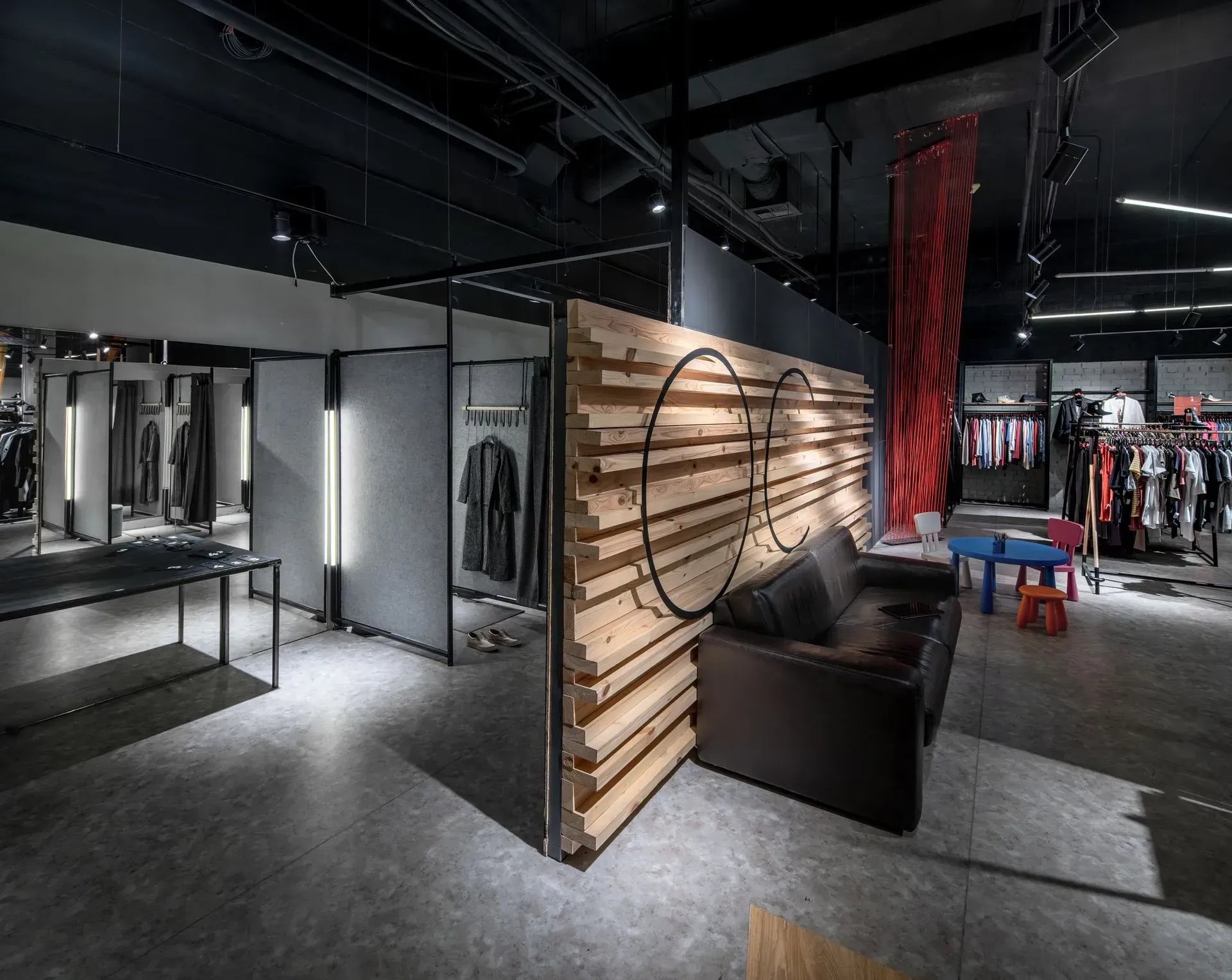 Modern clothing store interior with racks, mirrors, black seating, wood wall, and red hanging decor
