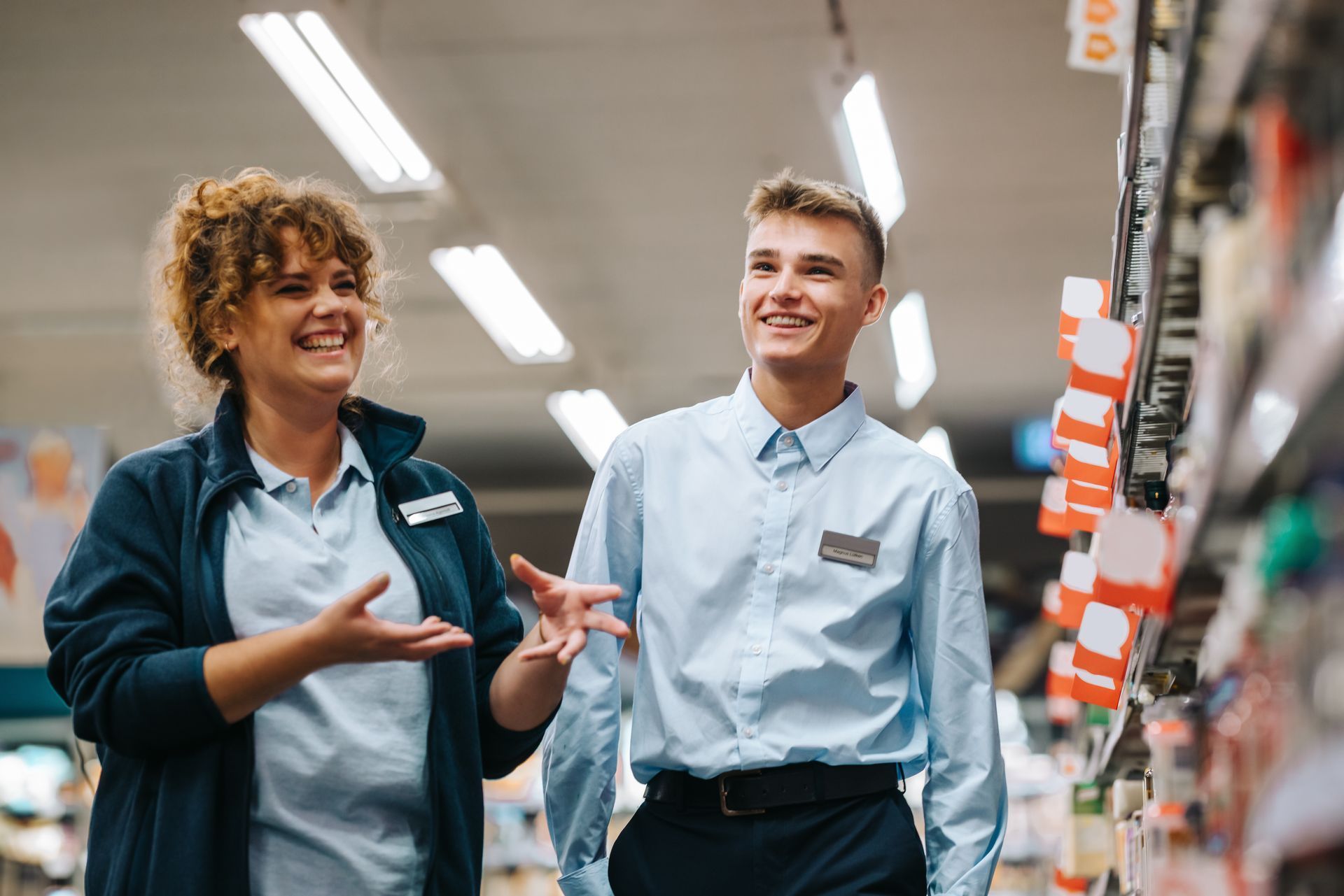 Two store employees smiling and talking in a brightly lit supermarket aisle