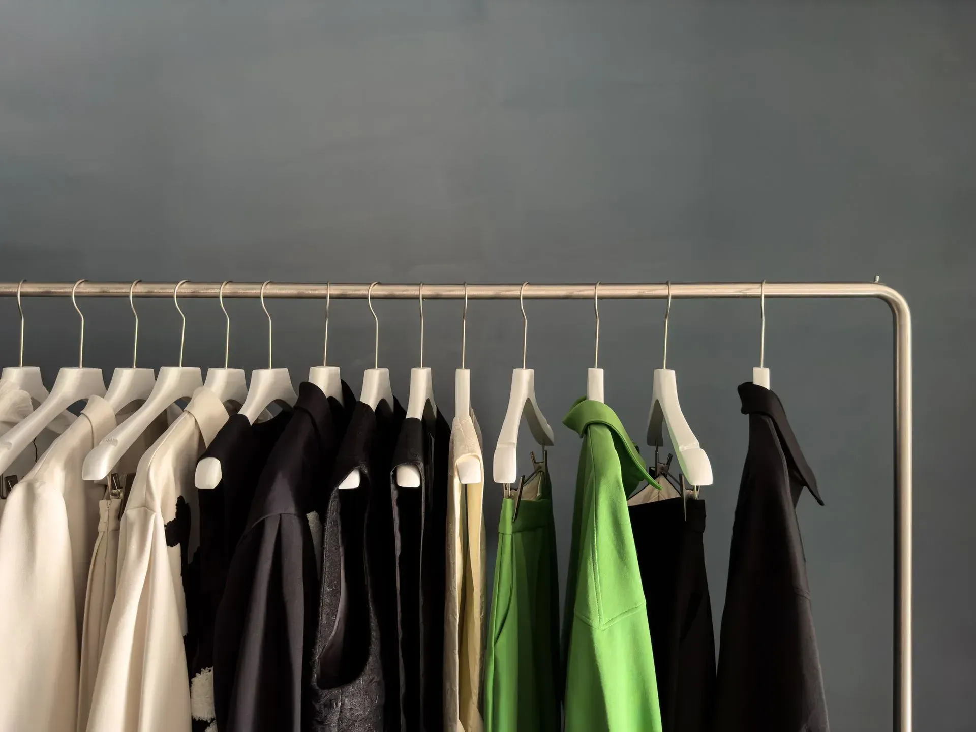 Clothing rack with assorted black, white, and green jackets on hangers against a gray wall