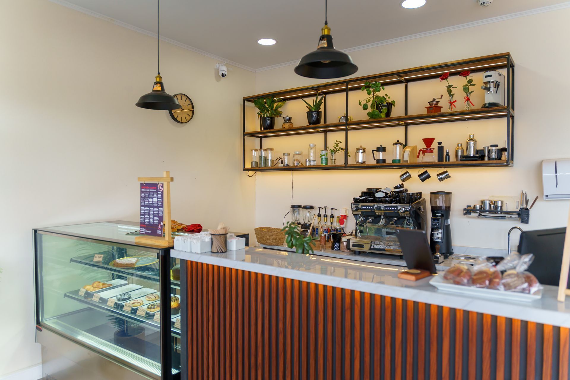 Bright café interior with a pastry display case, espresso machine, and wood-paneled counter