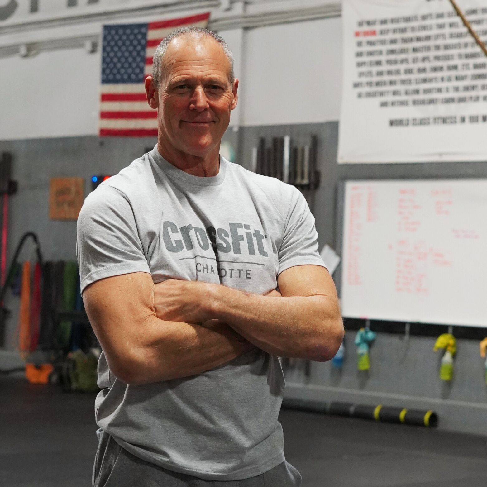 A man wearing a crossfit shirt is standing in a gym with his arms crossed