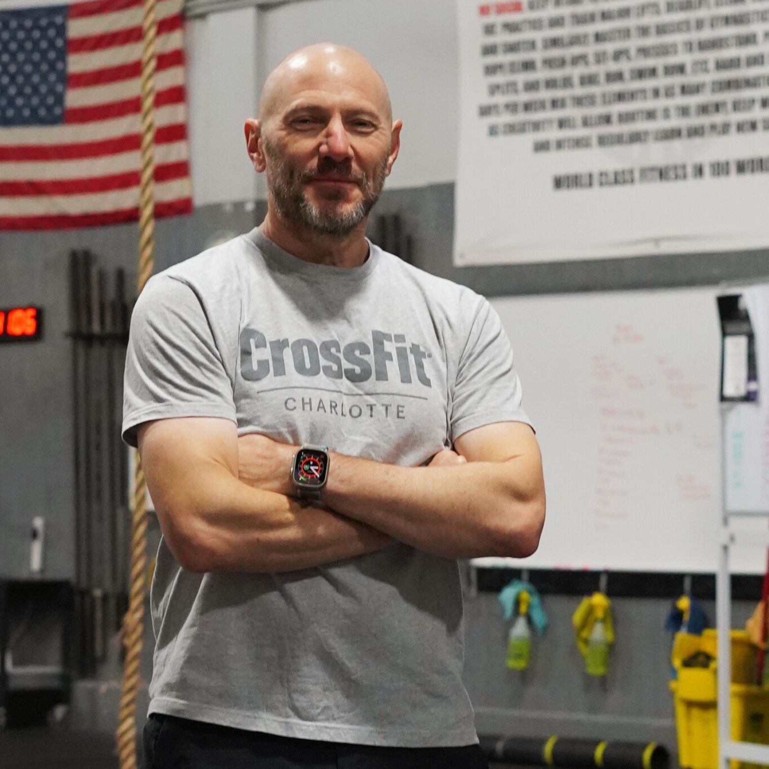 A man wearing a crossfit shirt is standing in a gym with his arms crossed