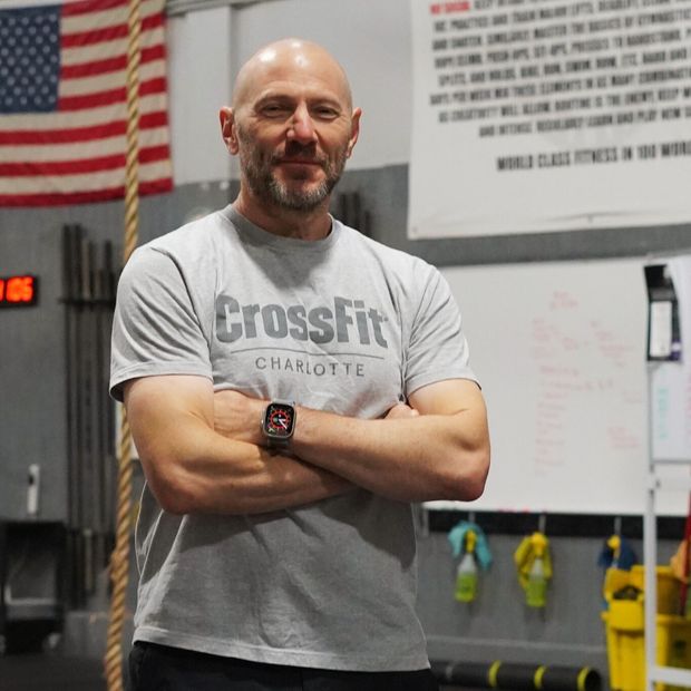 A man wearing a crossfit shirt is standing in a gym with his arms crossed