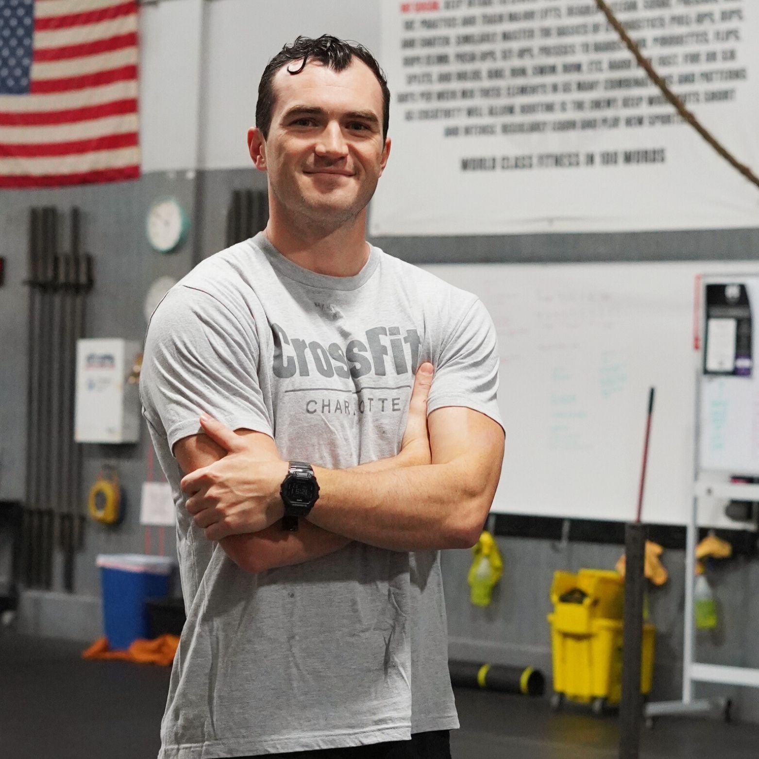 A man wearing a crossfit shirt stands with his arms crossed