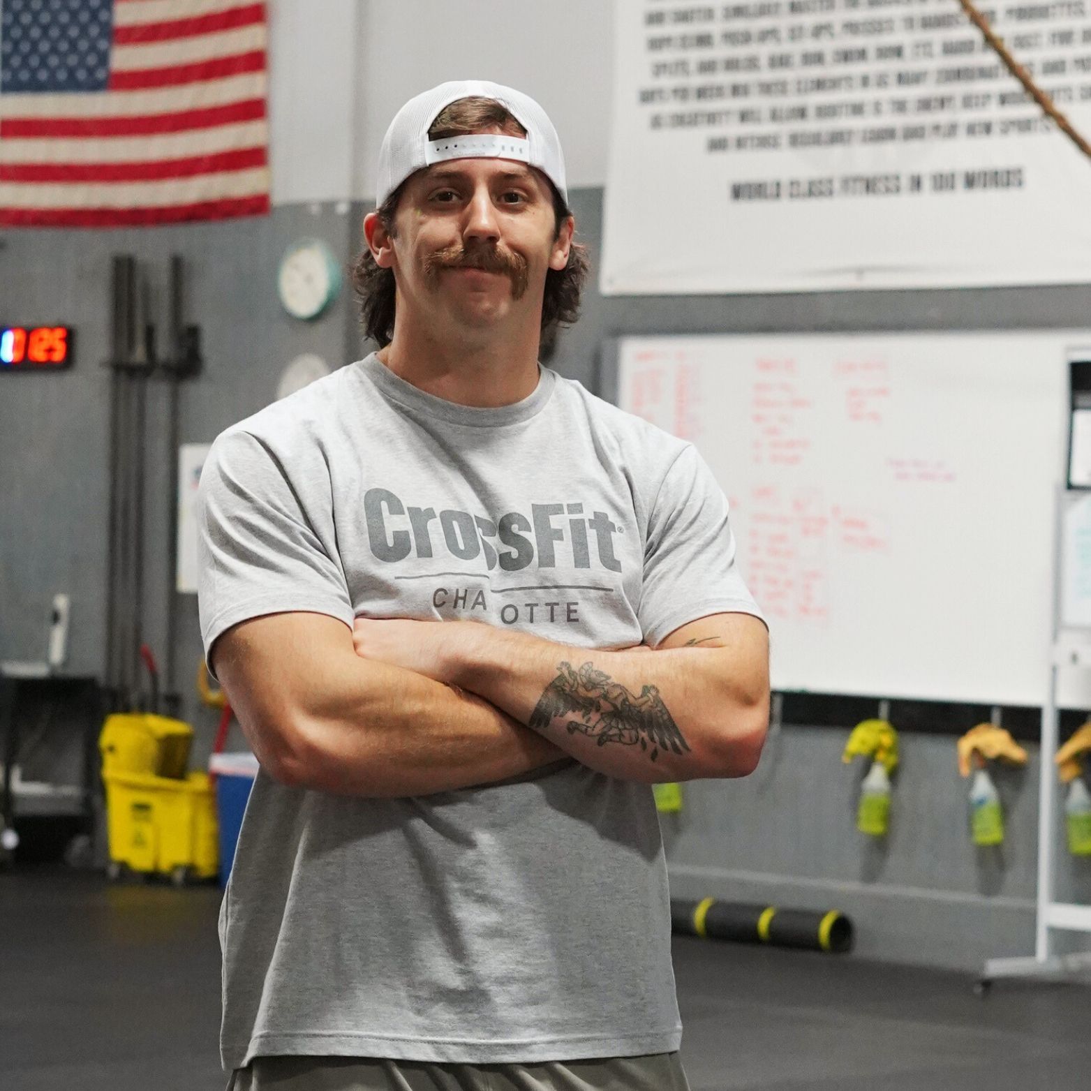 A man wearing a crossfit shirt stands with his arms crossed