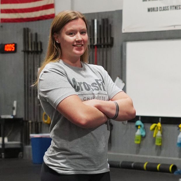 A woman wearing a crossfit shirt stands with her arms crossed