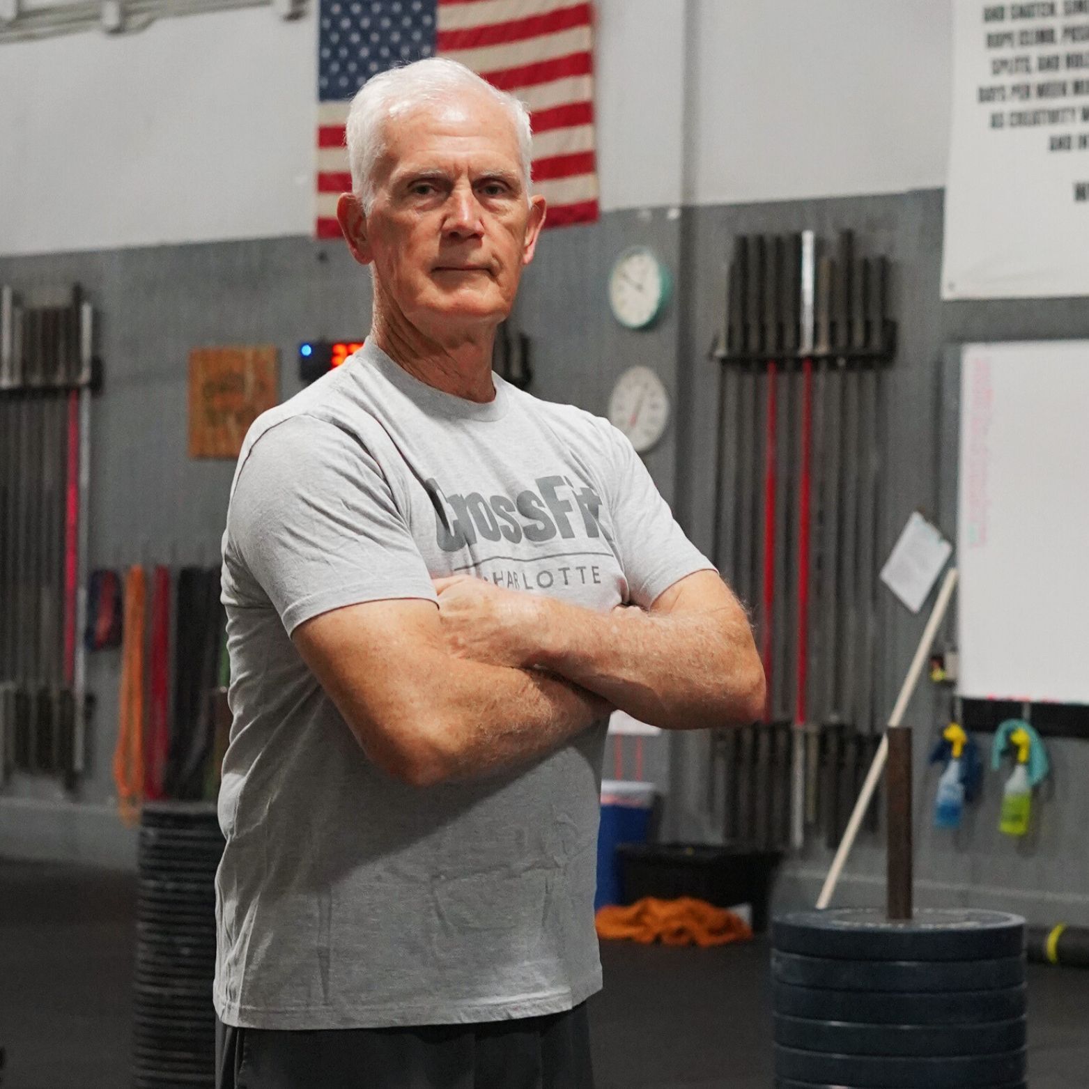 A man wearing a crossfit shirt is standing in a gym with his arms crossed