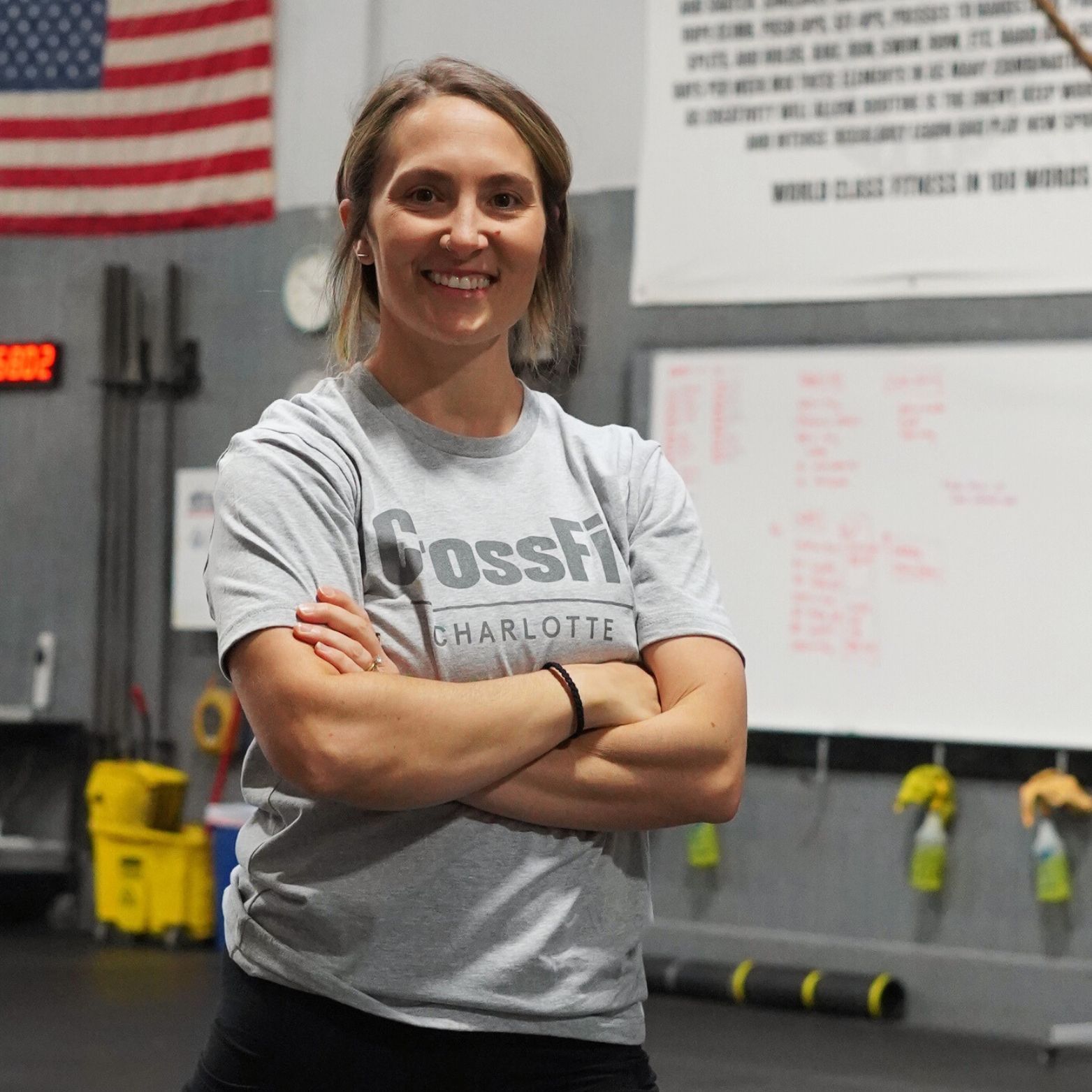 A woman wearing a crossfit shirt is standing with her arms crossed