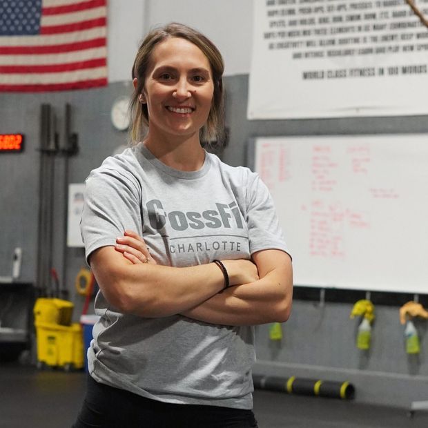 A woman wearing a crossfit shirt is standing with her arms crossed