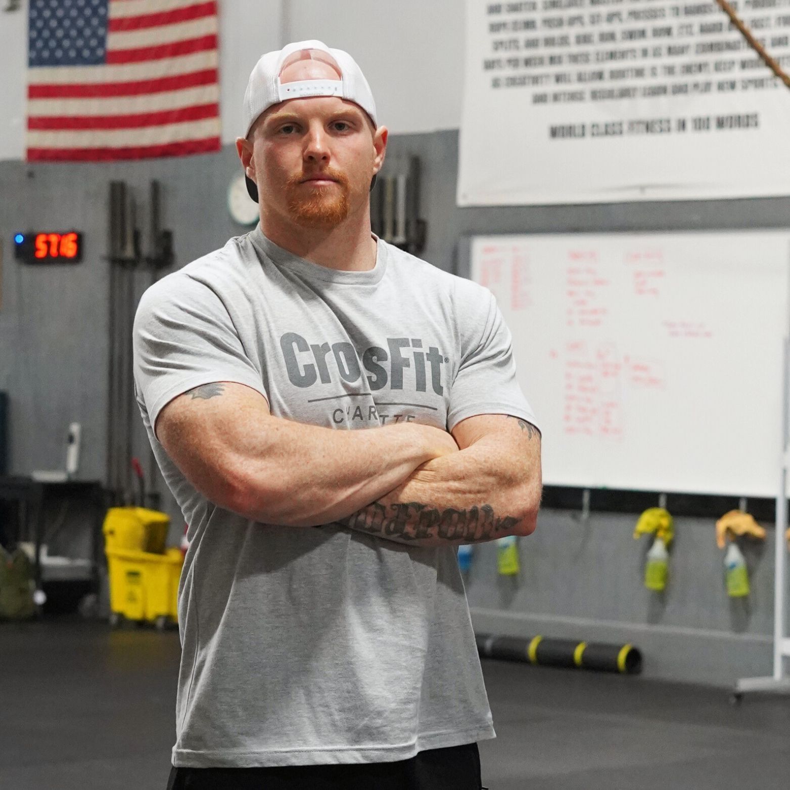 A man wearing a crossfit shirt stands with his arms crossed
