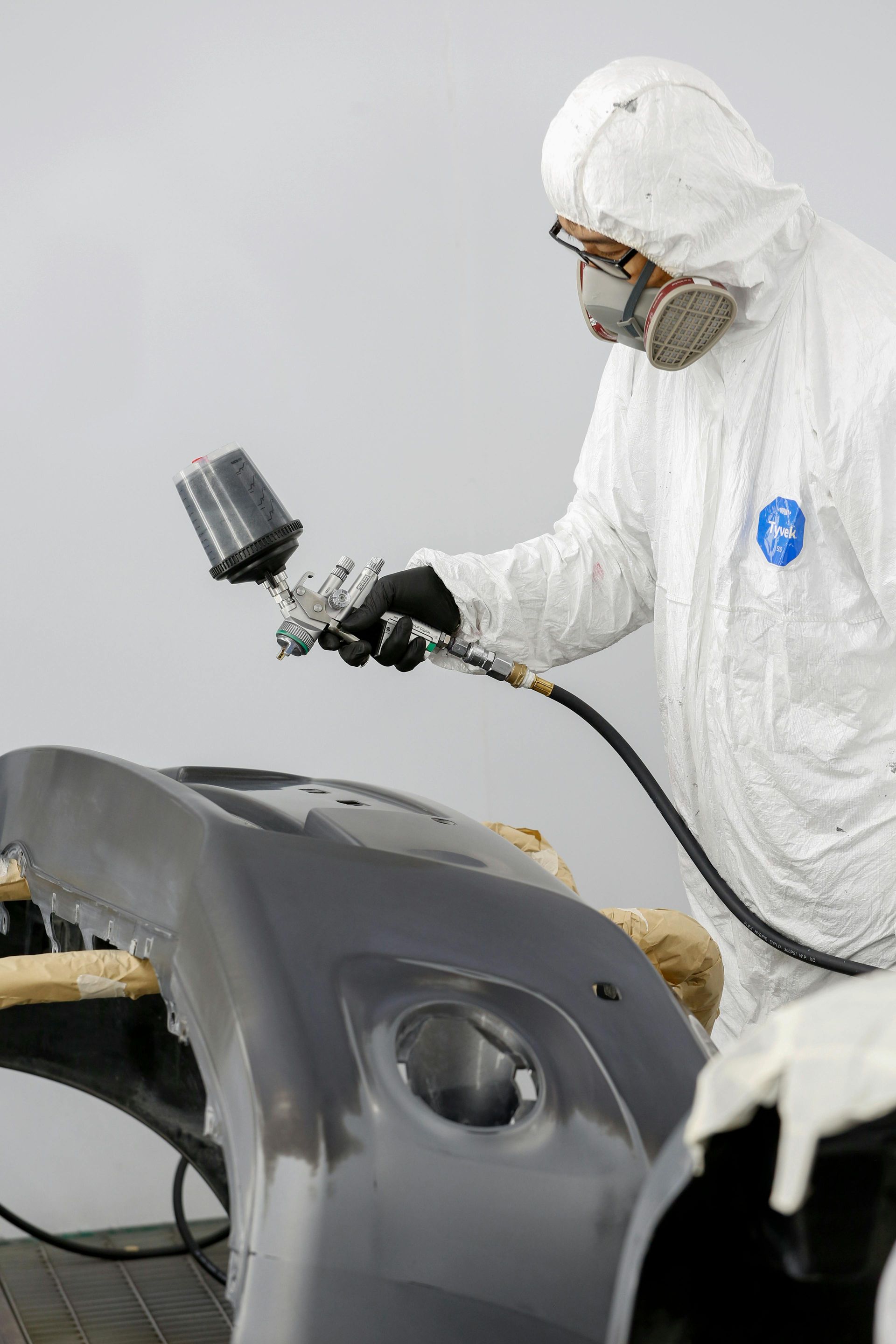 A man in a protective suit is spray painting a car bumper.